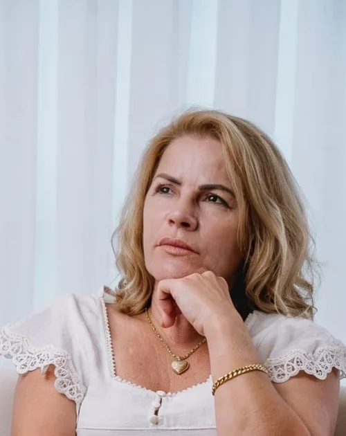 Cissa na poltrona, com a mão no queixo, diante da cortina branca